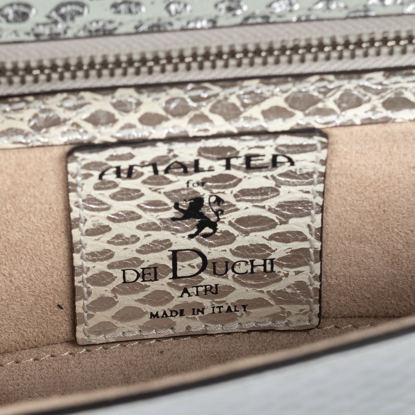 Close-up of a silvery snake textured leather bag with an ENGRAVED 'AMALTEA' branding on a leather patch on a white background. - DEI DUCHI (AMALTEA)
