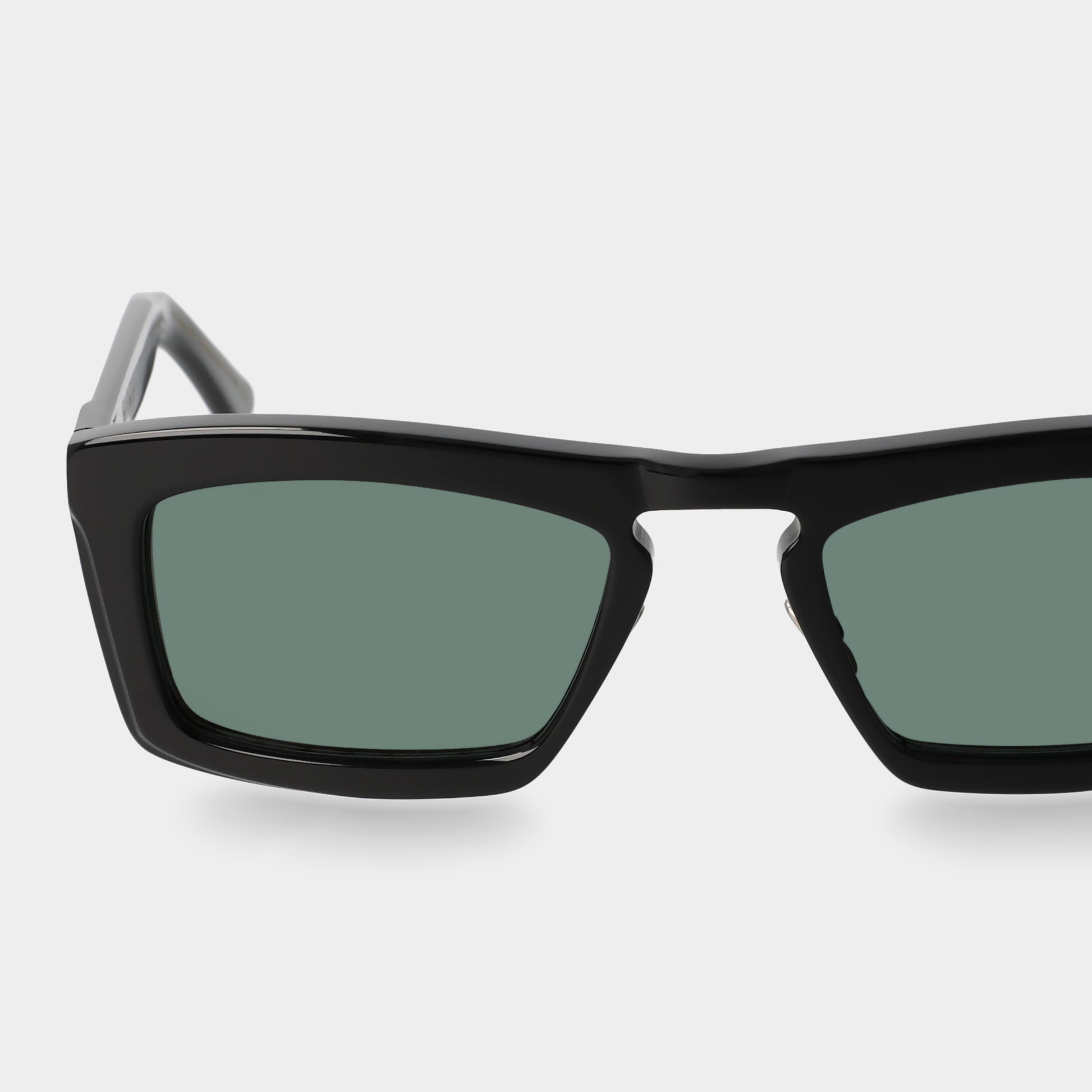 Black sunglasses with green lenses on a light gray background. - Dei Duchi
