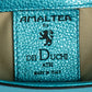 Close-up of a textured label with 'Amaltera for Dei Duchi Atri' branding on a teal background. DEI DUCHI (AMALTEA)