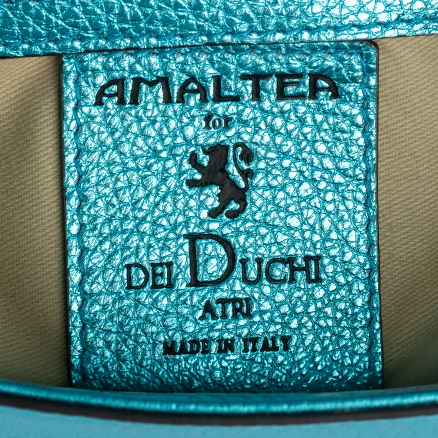 Close-up of a textured label with 'Amaltera for Dei Duchi Atri' branding on a teal background. DEI DUCHI (AMALTEA)