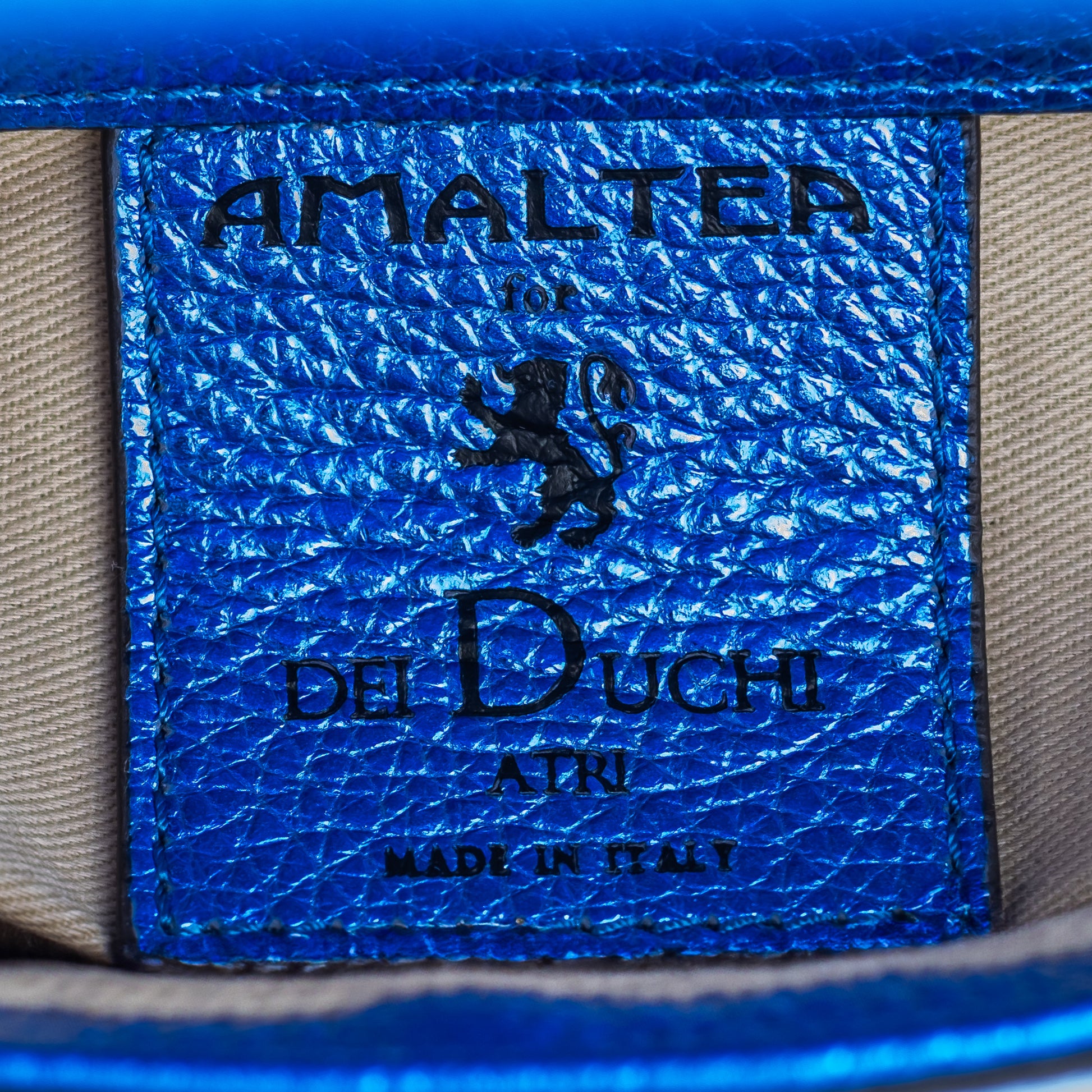 Close-up of a blue leather label with 'Amaltea for Del Duchi Atri' brand leather tag and logo. - DEI DUCHI (Amaltea)