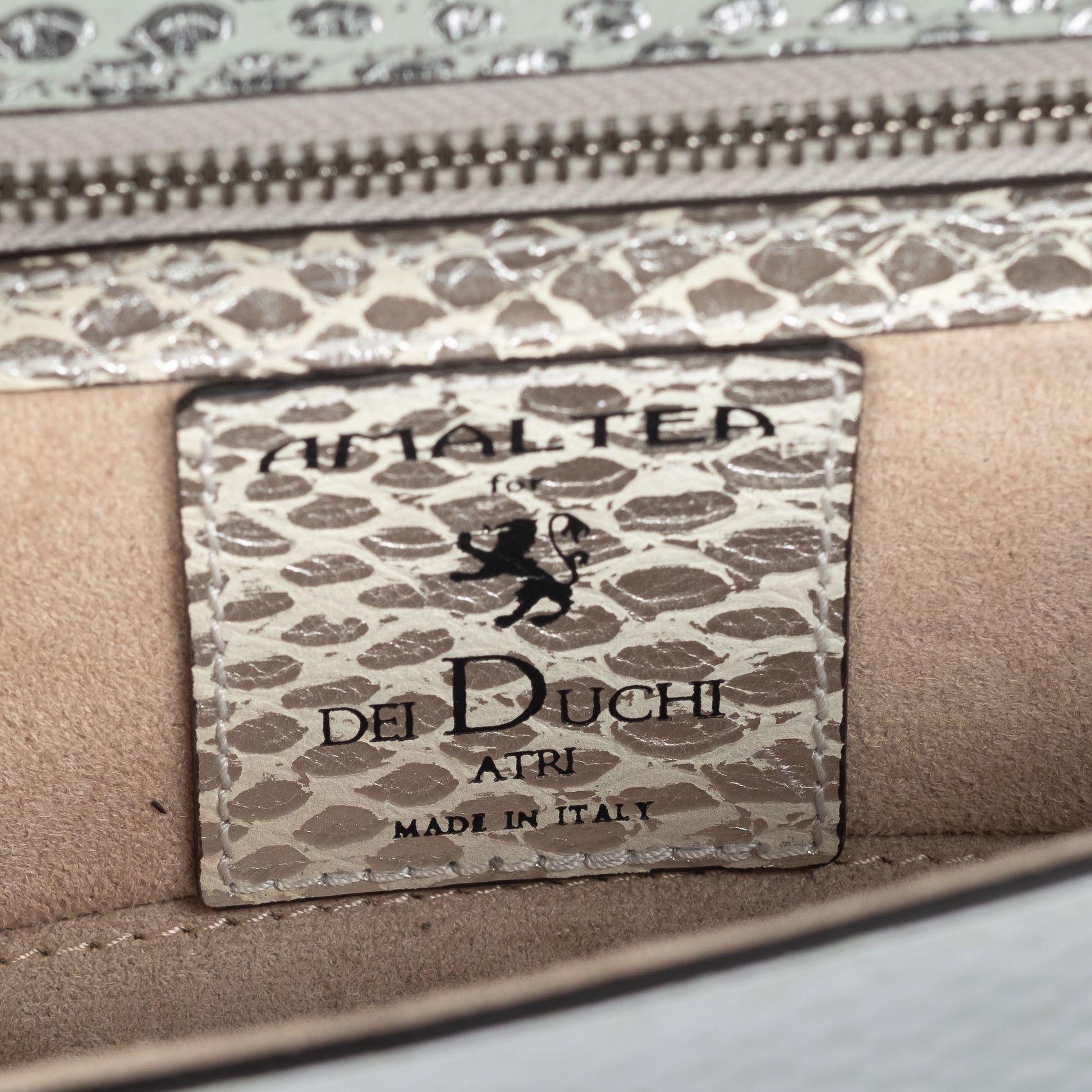 Close-up of a silvery snake textured leather bag with an ENGRAVED 'AMALTEA' branding on  a leather patch on a white background. - DEI DUCHI (AMALTEA)