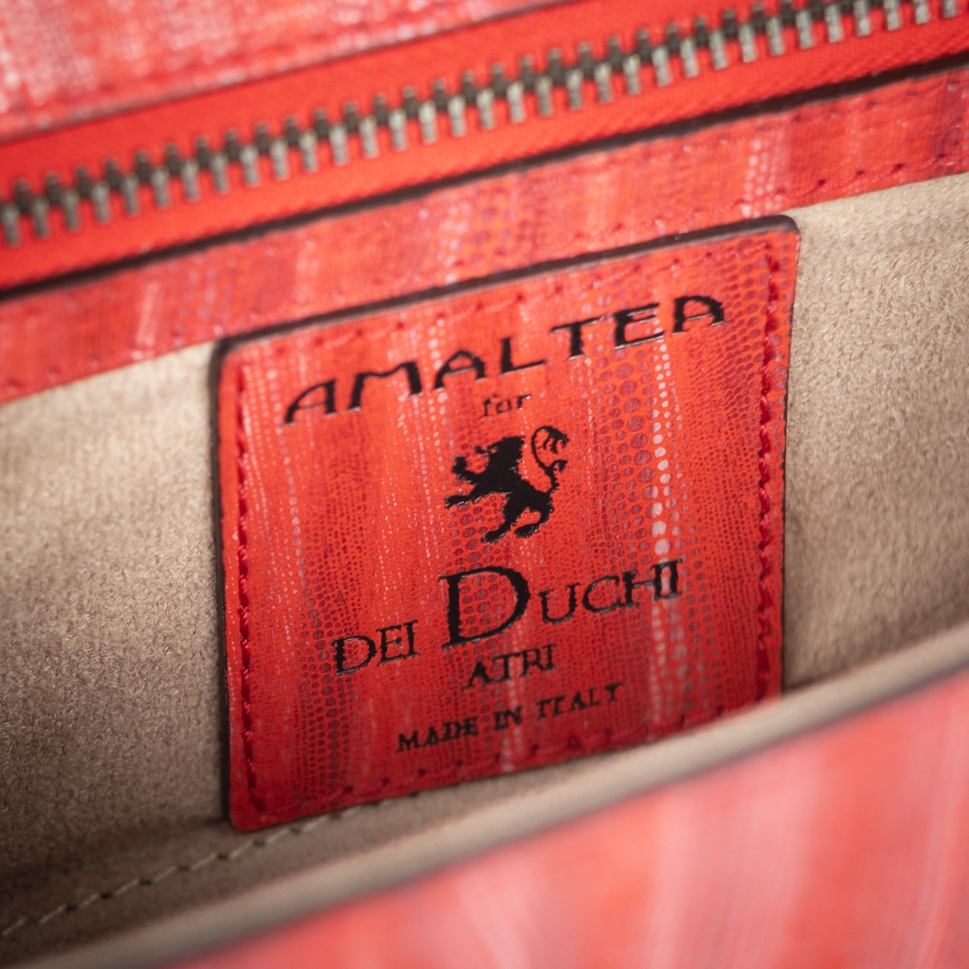 Close-up of a red leather label with 'Amaltea for Dei Duchi' branding on a leather bag product. - DEI DUCHI (AMALTEA)